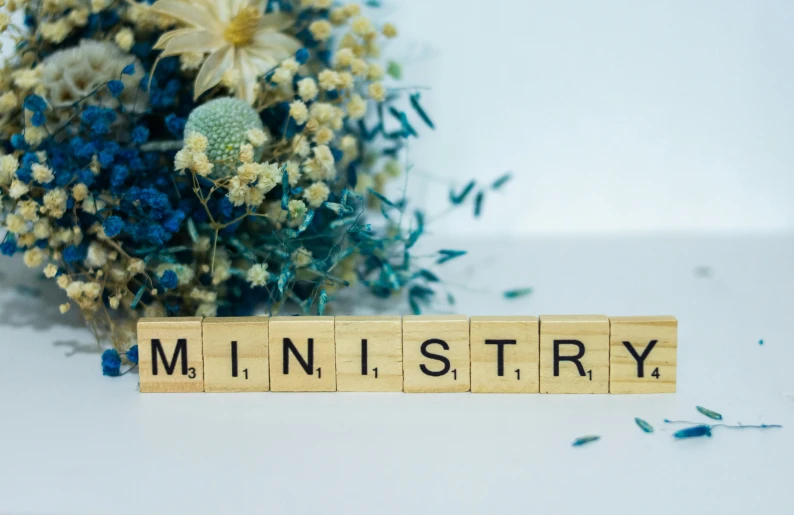 a scrabbled wooden block that reads miniatry with blue and white flowers beside it