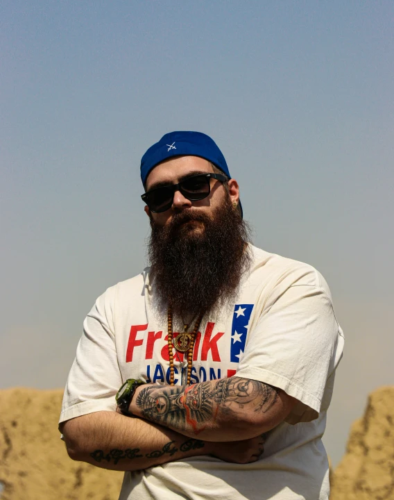 a man with a beard and tattoos wearing a hat and sunglasses