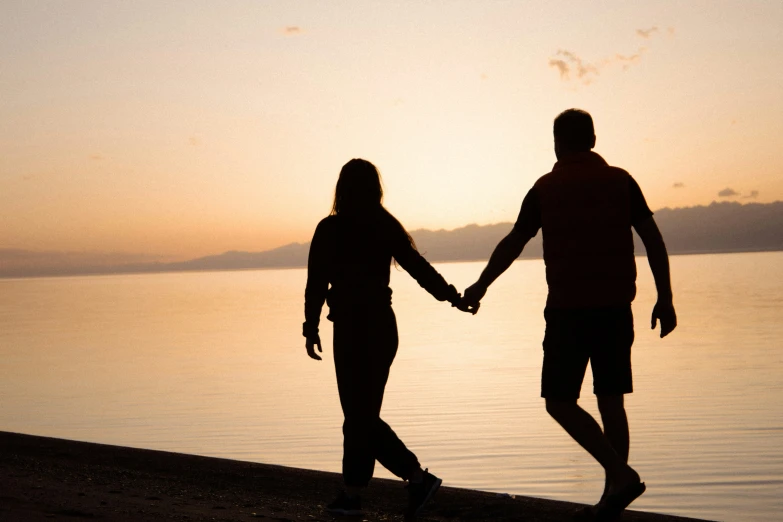 man and woman holding hands in front of water during sunset