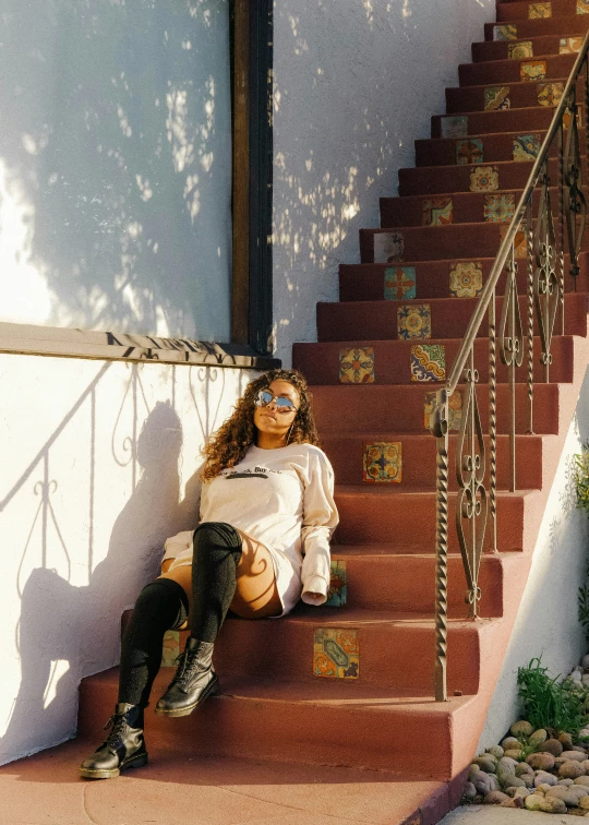 a woman in sunglasses sitting on stairs with her skateboard