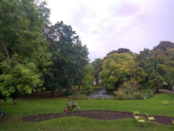 an open park that has several benches and chairs, with some people sitting on the bench