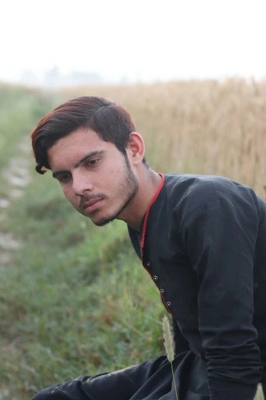 a man with brown hair sitting down next to a field