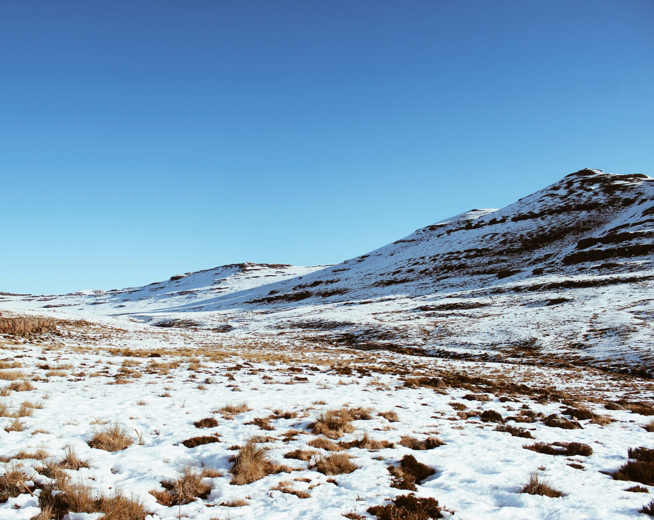 an empty field covered in snow with mountains and scrub brush