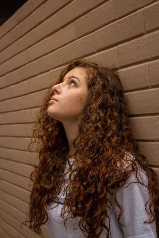 a woman standing against a brick wall with a piece of paper in her mouth