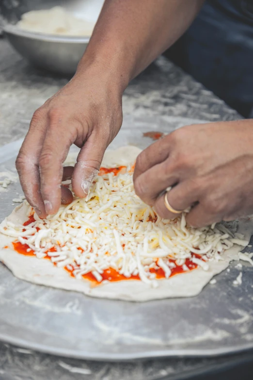two hands that are putting cheese on top of a pizza