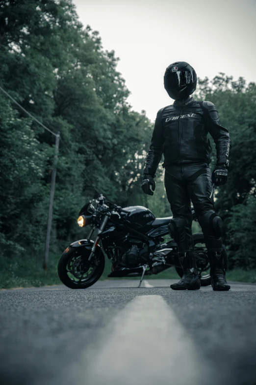 a person in black stands next to a motorcycle on a paved street