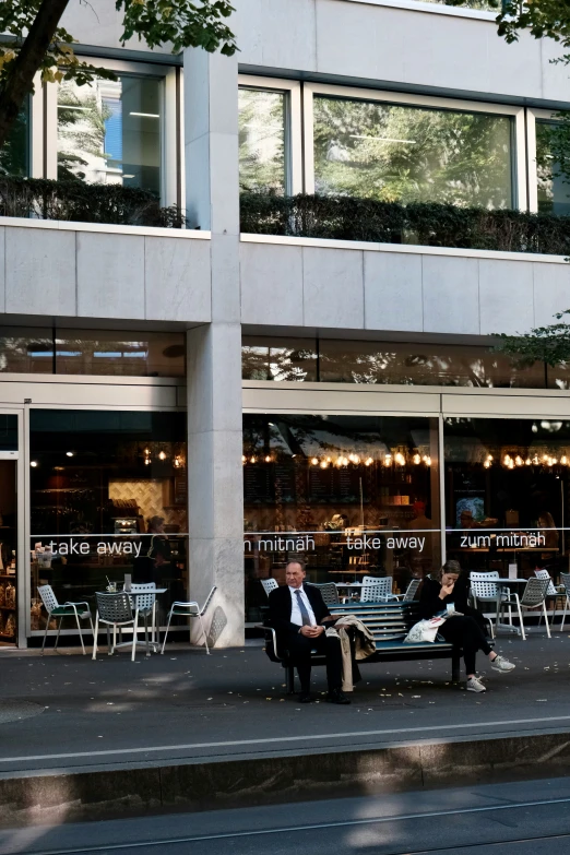 two people sitting on the bench in front of a coffee shop