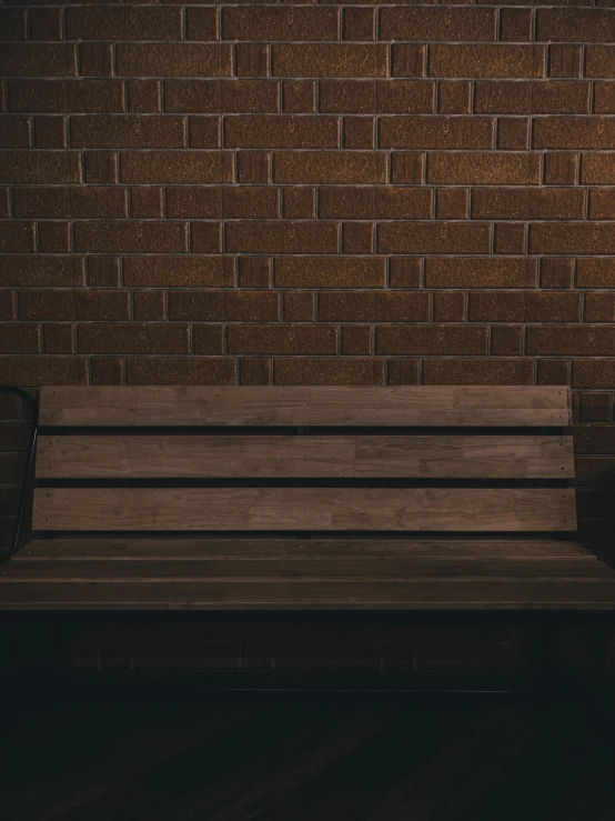 a lone bench with a brown brick wall behind it