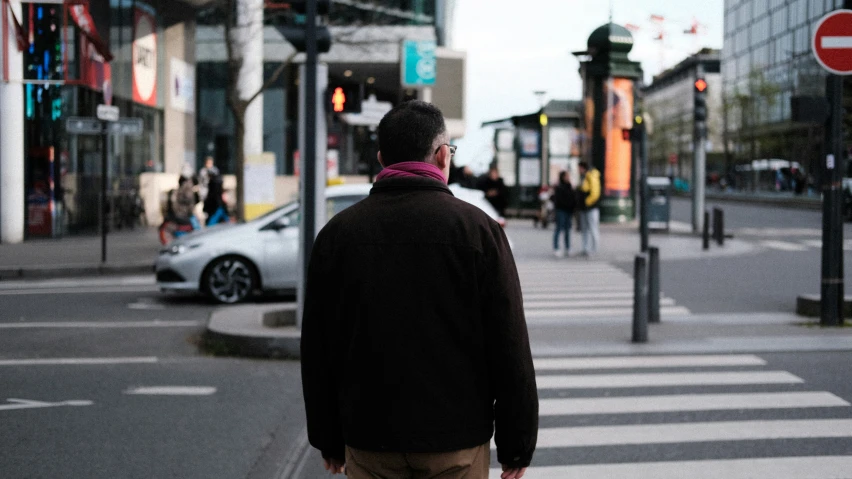 a man standing next to a road waiting at the cross walk