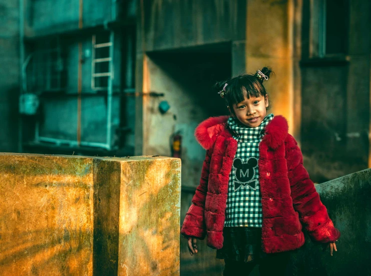 a young child standing against the fence of an old building