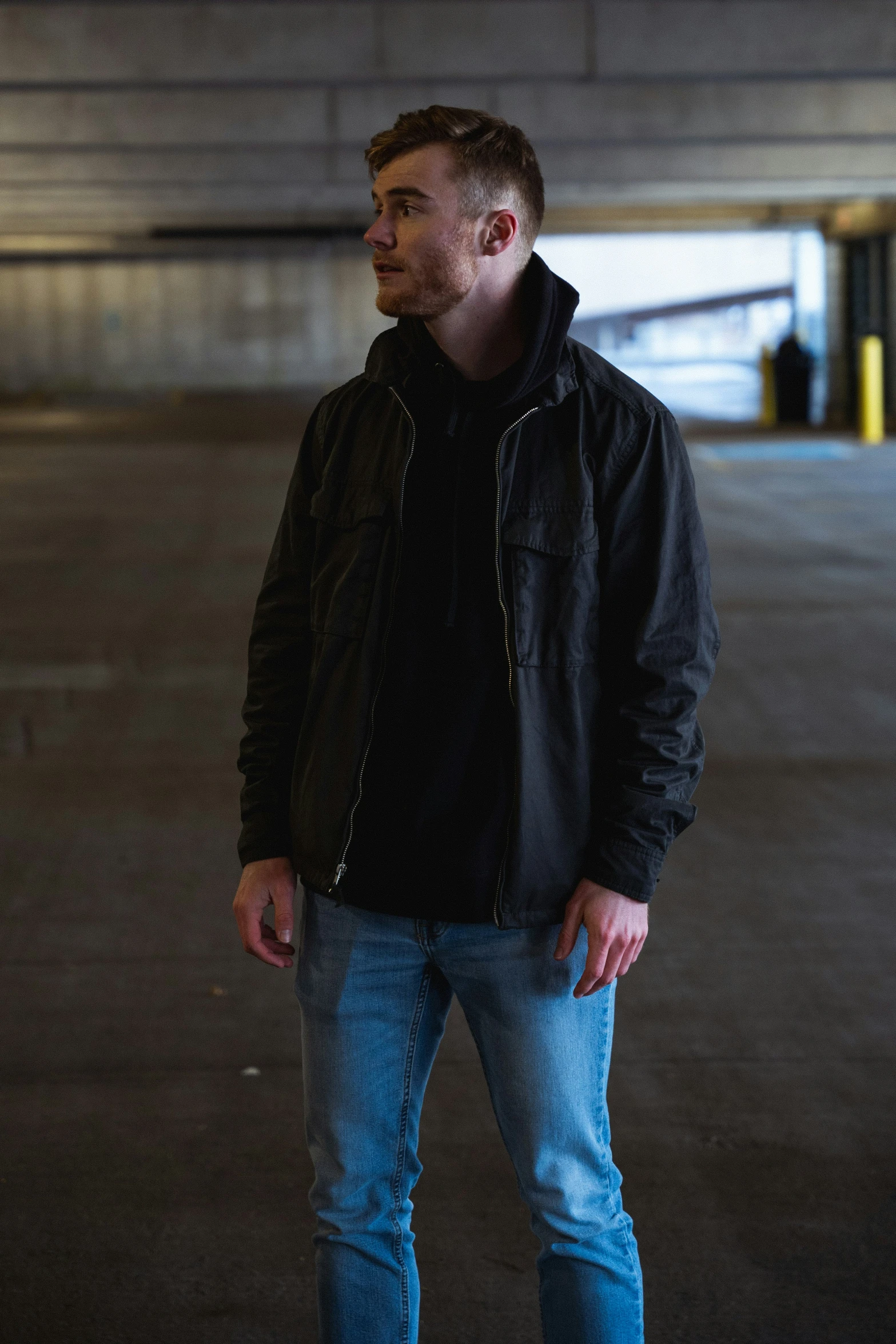 a young man with short hair is wearing blue jeans and black jacket