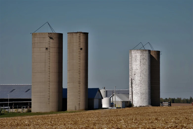 two large grain silos next to an empty barn