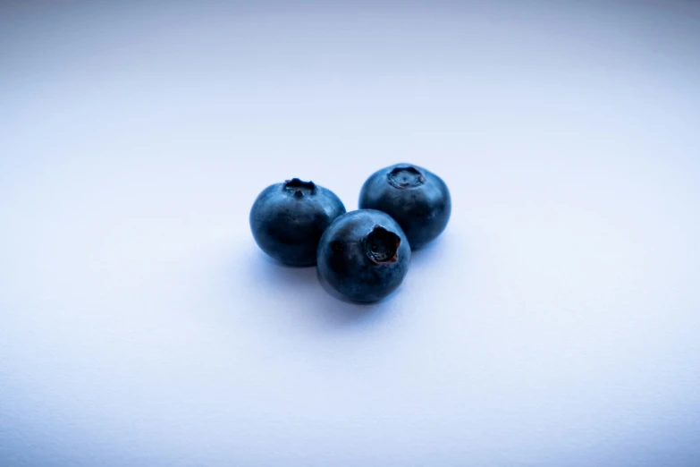 three fresh blueberries are on a white surface