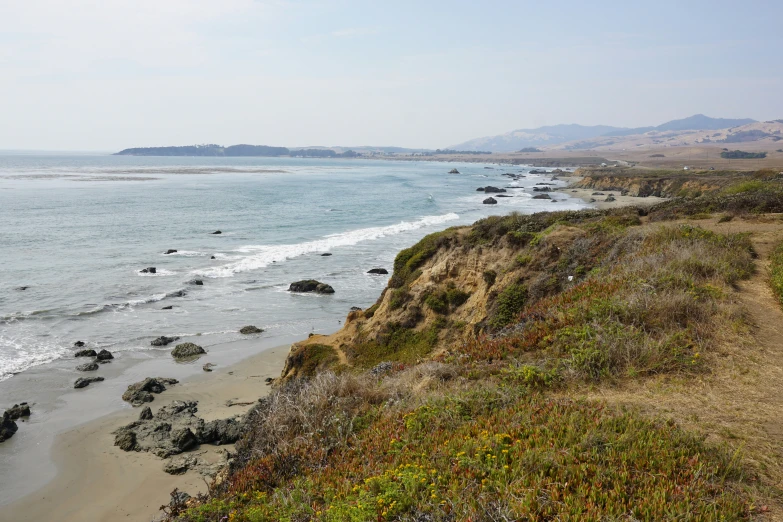 a sandy beach next to the ocean with water and hills in the distance