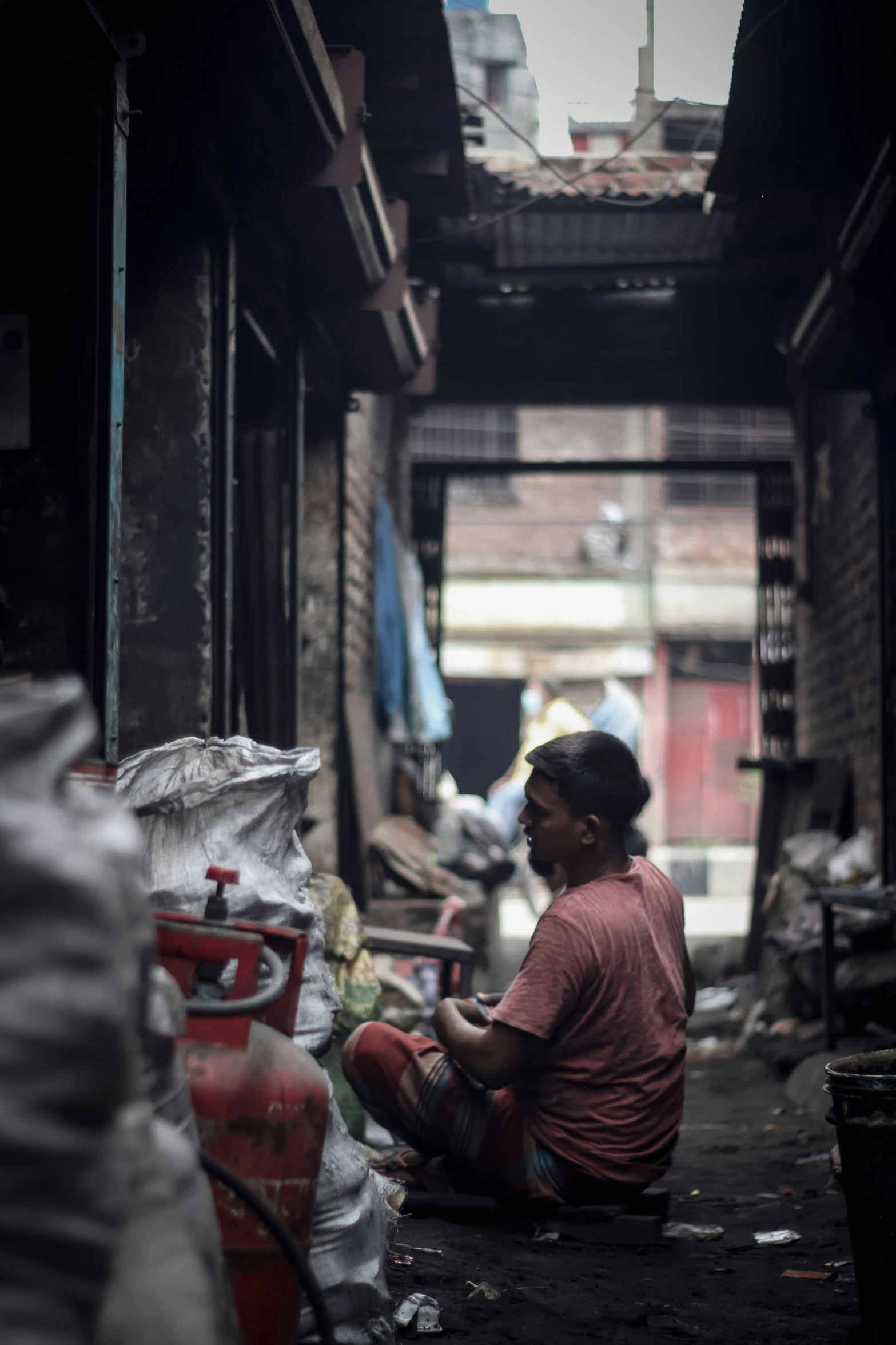 a young man sitting on the floor in a slum filled alley