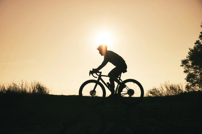 the silhouette of a person riding their bicycle on the hillside