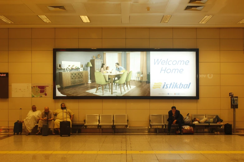 people waiting in line with luggage under large screen