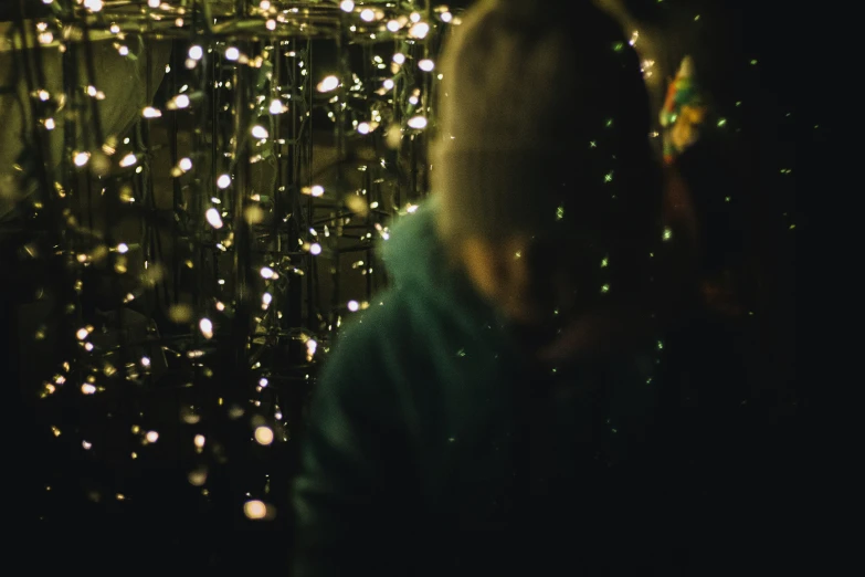 a girl is looking up at her cellphone while standing in front of a christmas tree with lights on it