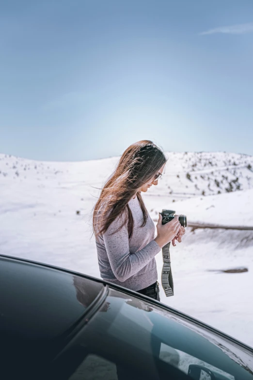 a young woman standing next to her car, looking at her cell phone