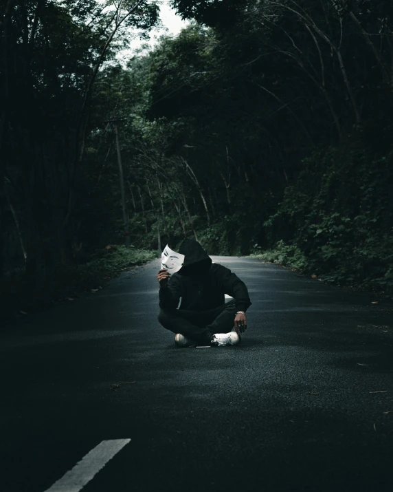 the person is squatting down on the street wearing a black hoodie