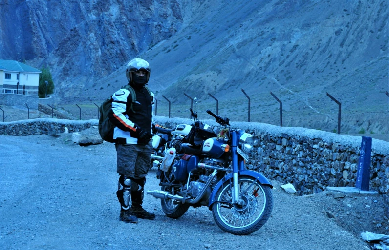 a man stands beside his motorbike while wearing goggles