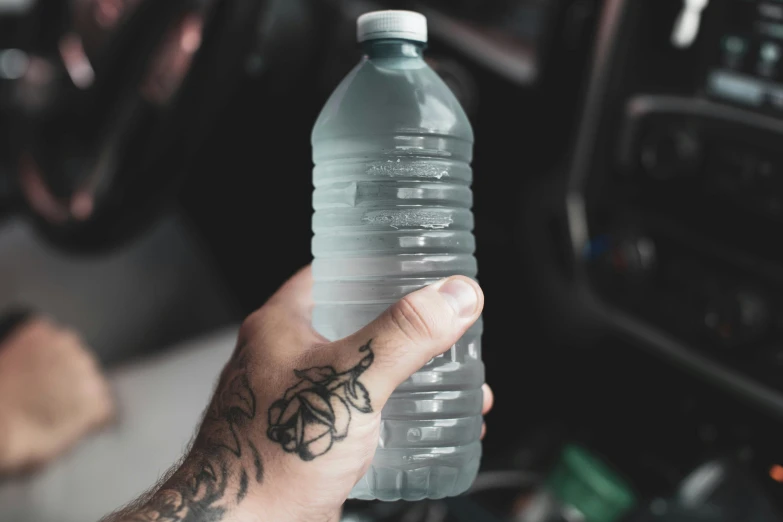 a man holds up a water bottle with a hand drawn tattoo