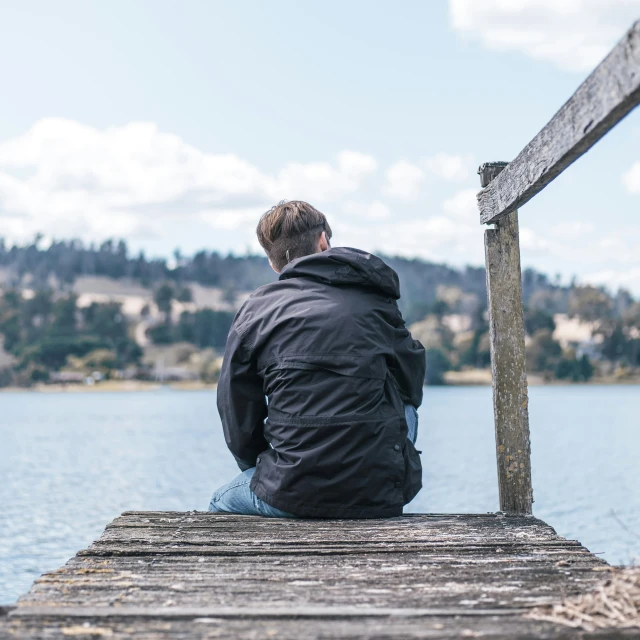 a man sitting on a wooden pier with his back to the camera