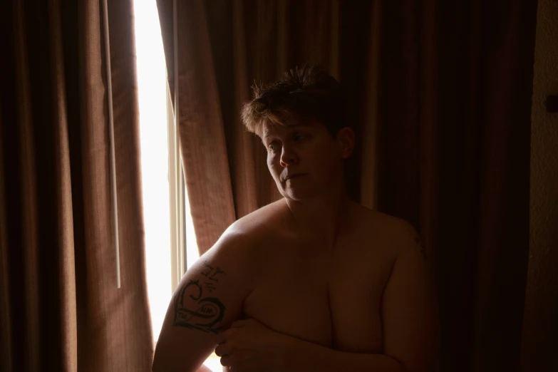 a shirtless man in a bathroom by the window