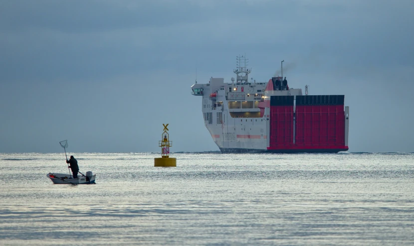 two people in a small boat on the water next to a huge cargo ship