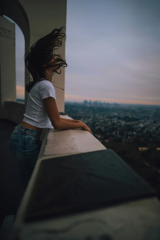 a woman standing at the edge of a balcony looking out over a city