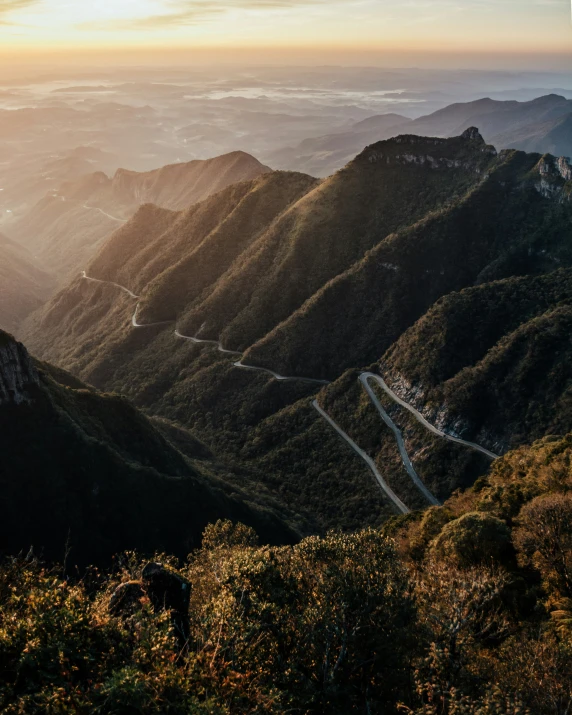 the sun is setting over mountains and road curves