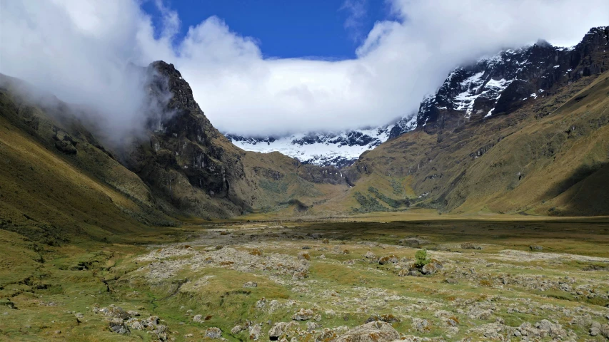 two mountains surrounded by grass and rocks under a cloudy blue sky