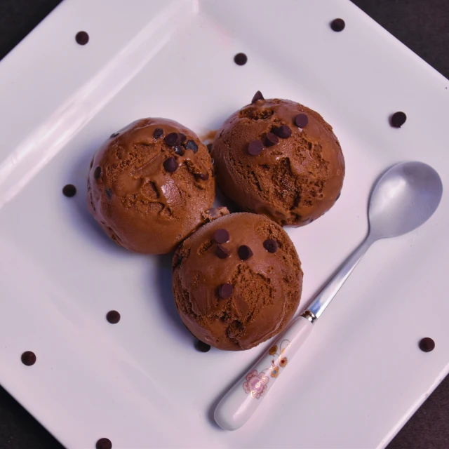 three muffins are on a white plate and a spoon sits next to them