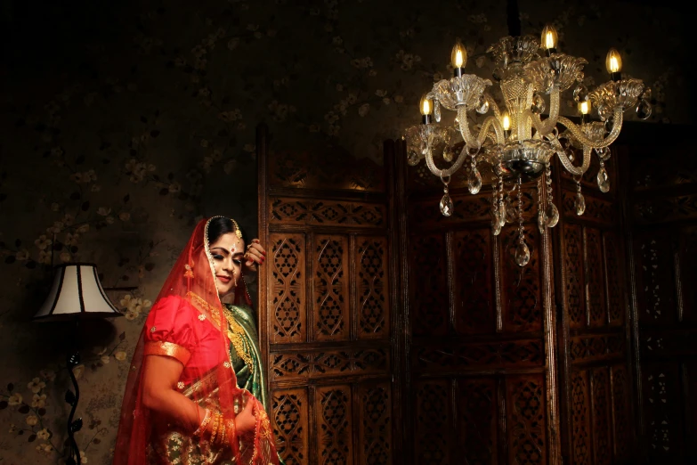 a beautiful woman wearing red and gold in a room with chandelier