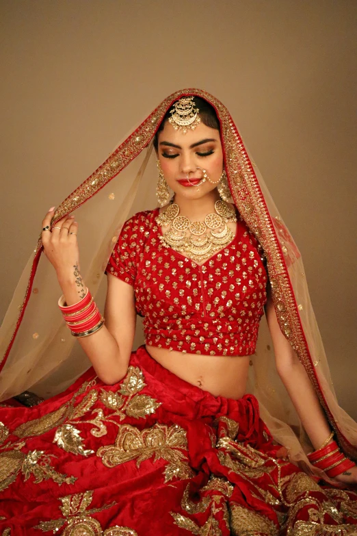 an indian woman in red and gold sitting with her head bowed in a veil