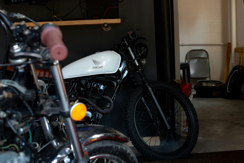 a motorcycle sits inside of a garage while another motorcycle is parked in the background