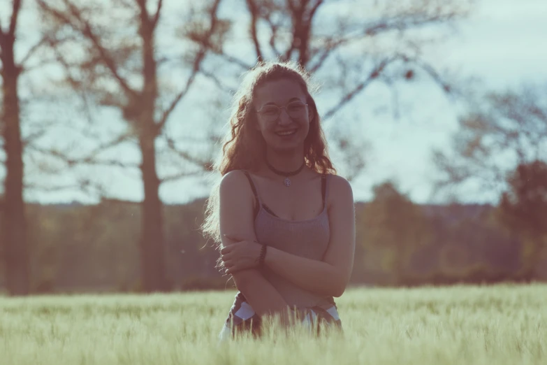 a girl with her arms crossed smiles in a field of grass