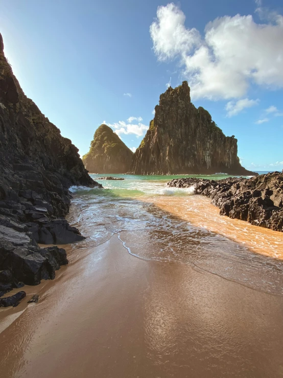 a sandy beach near some rocks and an ocean shore