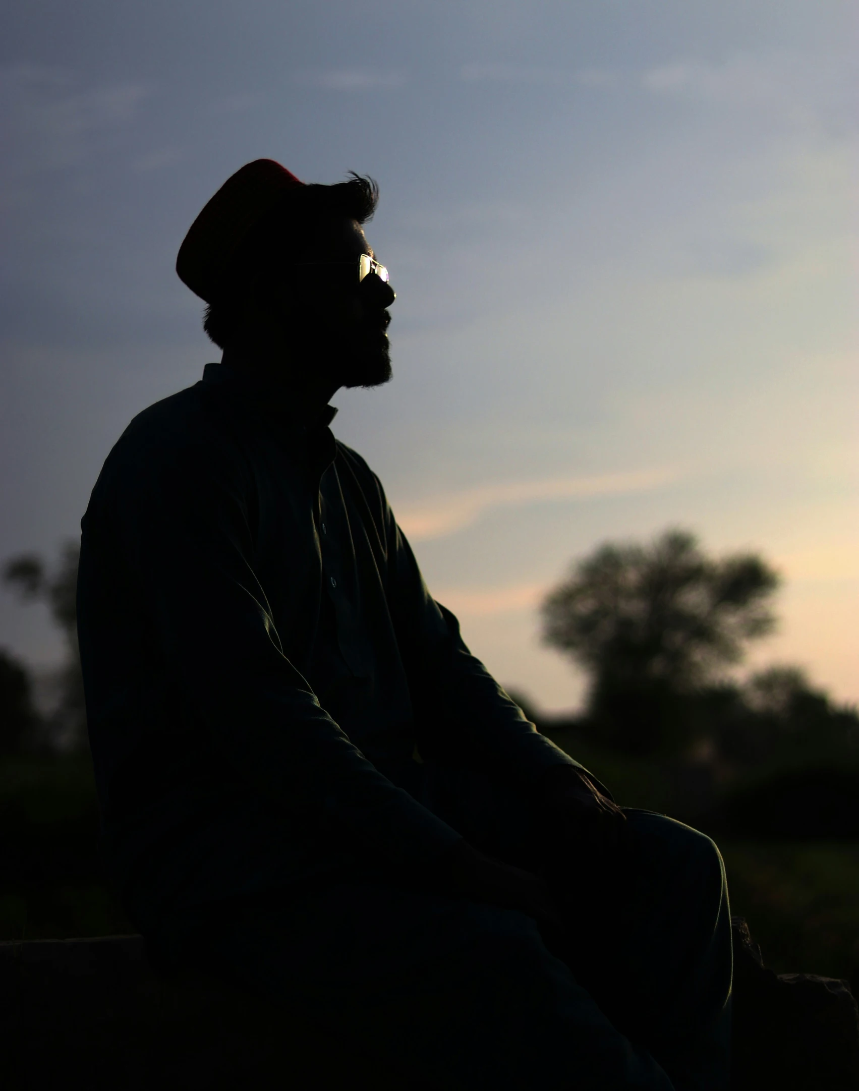 man in hat and sunglasses sitting in the sun at sunset