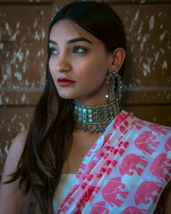 a woman wearing large silver earrings stands near a brick wall