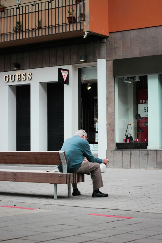 man sitting on wooden bench in front of storefront