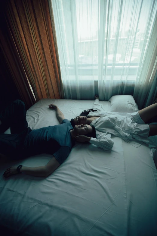 two people lie on a bed in front of a window