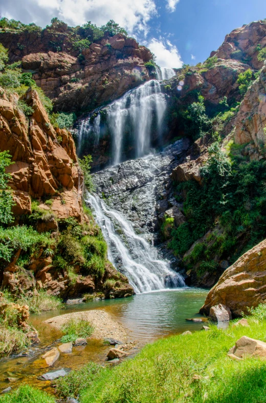 a waterfall in a mountain side setting with green grass and rocks