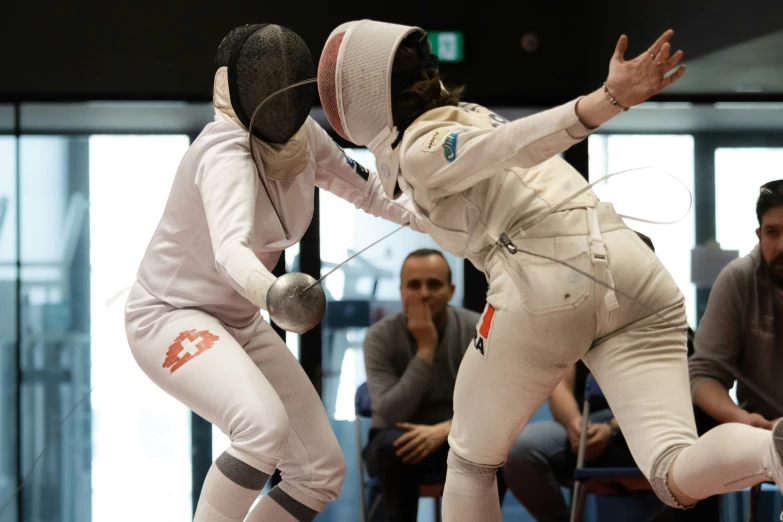 two people wearing white fencing gear are fighting in a court