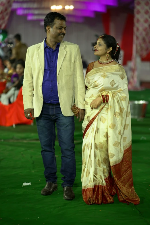 a man in a beige suit and woman in a sari walk on a green carpet
