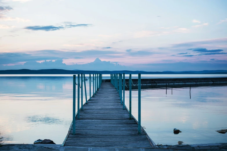 a pier on a body of water with water rocks and clouds