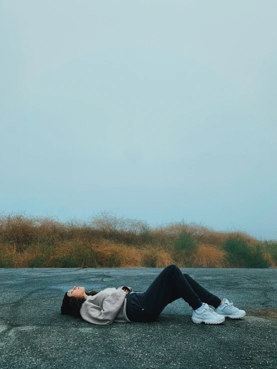 a person laying on a gravel road with a sky background