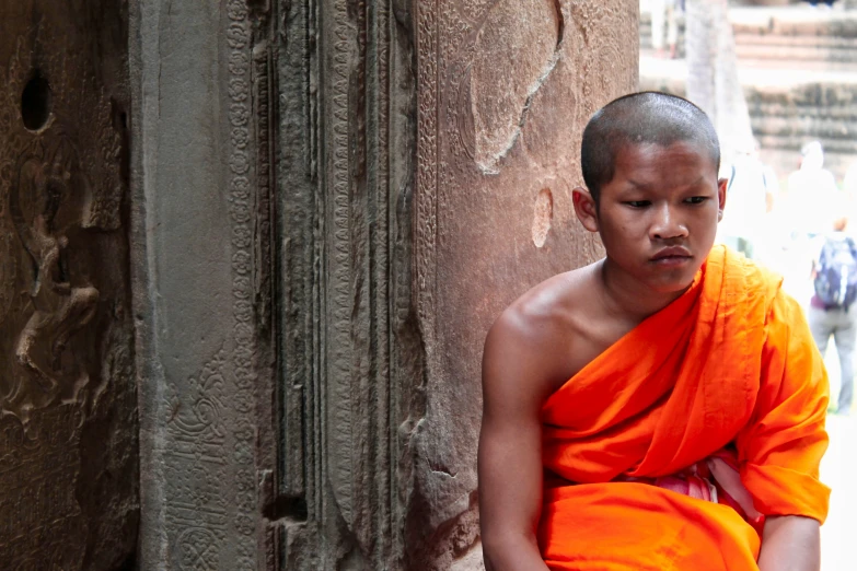 a boy dressed in orange sitting against a stone wall