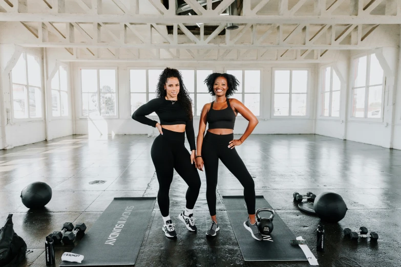 two women standing on an exercise mat with equipment in front of them