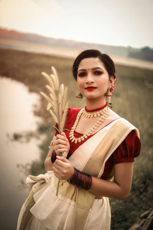 the woman is standing next to a body of water with some flowers in her hand